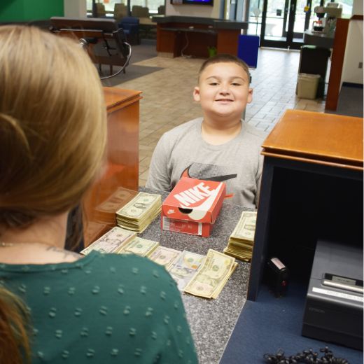 Young boy at teller with piles of cash to deposit
