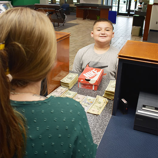 Young boy at teller with piles of cash to deposit