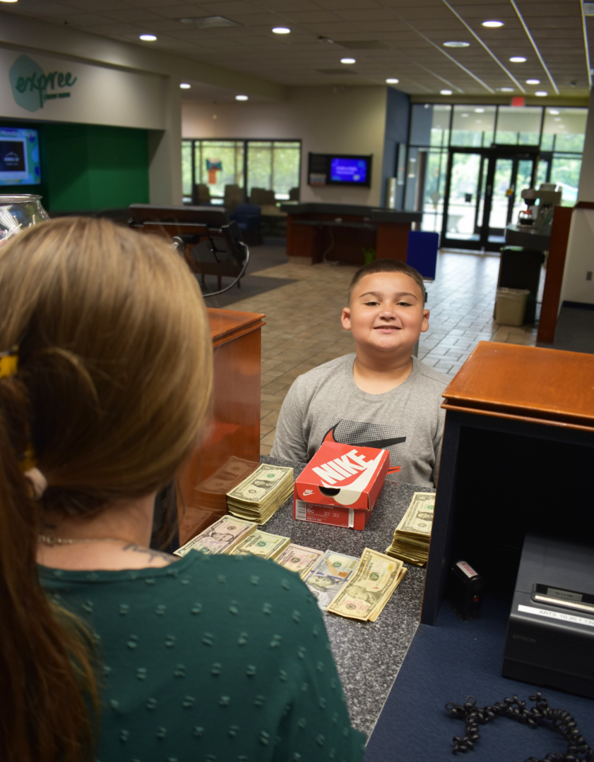 Young boy at teller with piles of cash to deposit